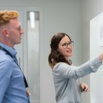 Two people standing at a whiteboard discussing implementing an account planning strategy
